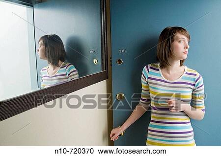 Stock Image - Young woman standing in front of her apartment door.. Fotosearch