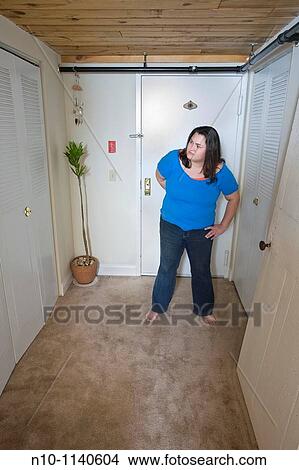 Picture - Young woman standing in her apartment hallway. Fotosearch