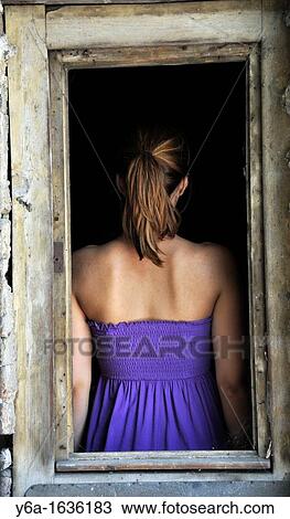 Stock Image - Young woman standing in window frame rear view. Fotosearch