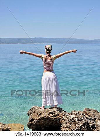 Young woman standing on rocks by ocean, arms raised View Large Photo Image Stock Image - Young woman standing on rocks by ocean, arms raised. Fotosearch