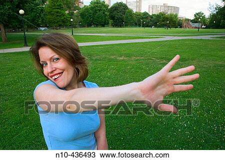 Young woman, standing on the grass at a park, dramatically waving her hand. View Large Photo Image Stock Image - Young woman, standing on the grass at a park, dramatically waving her hand.. Fotosearch