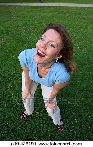Stock Photo - Young woman, standing on the grass at a park, dramatically expressing herself.. Fotosearch