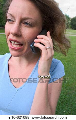 Young woman, standing on the grass at a park, talking on her cell phone. View Large Photo Image Stock Photo - Young woman, standing on the grass at a park, talking on her cell phone.. Fotosearch