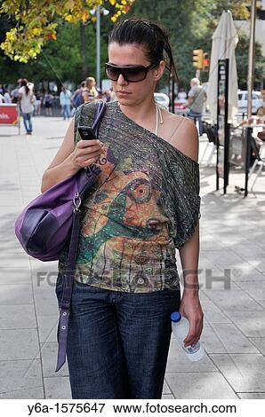 Stock Photo - Young woman standing outdoors text messaging. Fotosearch