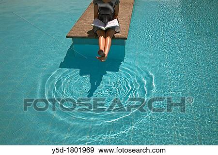 young woman studing, sitting at the poolside, with book on her knees and legs up above the water, round patterns of touching the water by legs, calm scenery View Large Photo Image Stock Photo - young woman studing, sitting at the poolside, with book on her knees and legs up above the water, round patterns of touching the water by legs, calm scenery. Fotosearch