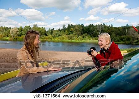 Young woman taking picture of happy smiling posing friend by car View Large Photo Image Picture - Young woman taking picture of happy smiling posing friend by car. Fotosearch