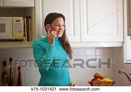 young woman talking on cell phone in kitchen View Large Photo Image Stock Image - young woman talking on cell phone in kitchen. Fotosearch
