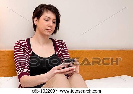 Young woman teenager sitting on bed using mobile phone View Large Photo Image Stock Photo - Young woman teenager sitting on bed using mobile phone. Fotosearch
