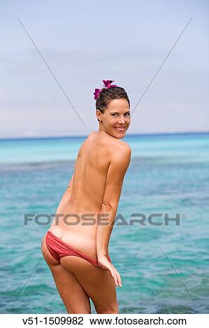 Stock Image - Young woman undressing on beach. Fotosearch