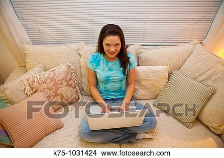 Picture - young woman using her laptop on couch. Fotosearch