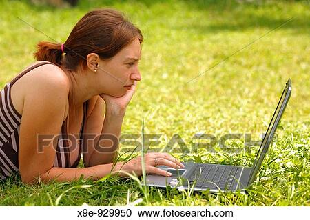 Stock Image - Young woman using her laptop outdoors. Fotosearch