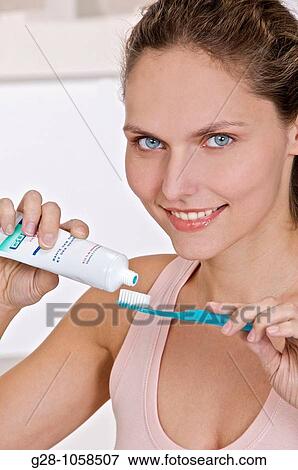 Stock Photo - young woman using her toothbrush and toothpaste in the bathroom for tooth hygiene. Fotosearch