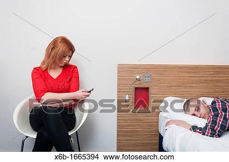 Young woman using mobile phone while her partner is asleep View Large Photo Image Picture - Young woman using mobile phone while her partner is asleep. Fotosearch