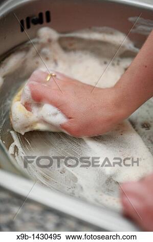 Stock Photography - Young woman washing dishes in the kitchen sink. Fotosearch