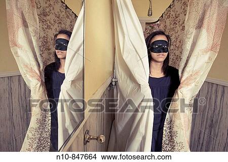Young woman, wearing a black mask, and her reflection, standing in her bathtub. View Large Photo Image Picture - Young woman, wearing a black mask, and her reflection, standing in her bathtub.. Fotosearch