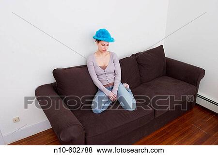 Stock Photo - Young woman, wearing a blue hat, sitting on a sofa.. Fotosearch