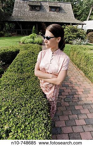 Young woman, wearing a gown and sunglasses, standing in a garden at a park. View Large Photo Image Stock Photography - Young woman, wearing a gown and sunglasses, standing in a garden at a park.. Fotosearch