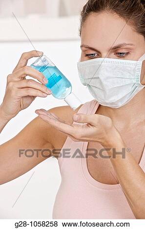 young woman wearing a mask, a nurse, holding a small bottle of blue desinfectant for hands ready to apply it to kill germs View Large Photo Image Stock Photo - young woman wearing a mask, a nurse, holding a small bottle of blue desinfectant for hands ready to apply it to kill germs. Fotosearch
