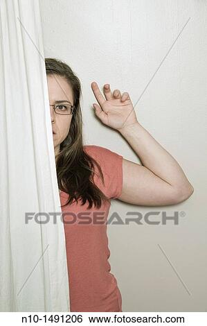 Young woman, wearing glasses, looking out from behind a curtain View Large Photo Image Stock Photograph - Young woman, wearing glasses, looking out from behind a curtain. Fotosearch