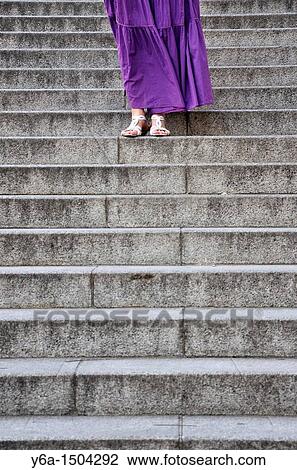 Stock Image - Young woman wearing purple dress standing on steps. Fotosearch