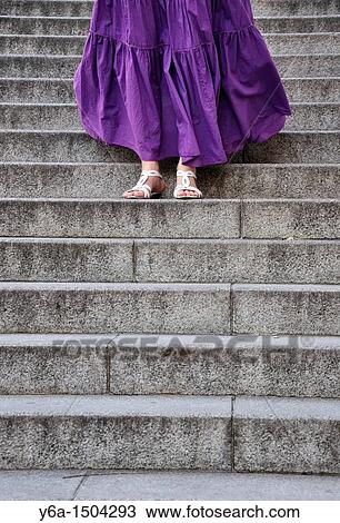 Stock Image - Young woman wearing purple dress standing on steps. Fotosearch