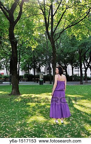Young woman wearing purple dress standing in a park outdoors View Large Photo Image Stock Image - Young woman wearing purple dress standing in a park outdoors. Fotosearch