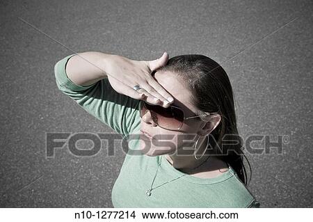 Young woman, wearing sunglasses, blocking the sun with her hand View Large Photo Image Picture - Young woman, wearing sunglasses, blocking the sun with her hand. Fotosearch