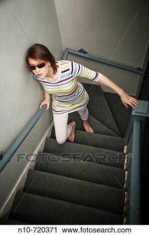 Stock Image - Young woman, wearing sunglasses, climbing her apartment building's stairs.. Fotosearch