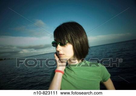 Young woman, wearing sunglasses, standing by the ocean. View Large Photo Image Stock Image - Young woman, wearing sunglasses, standing by the ocean.. Fotosearch