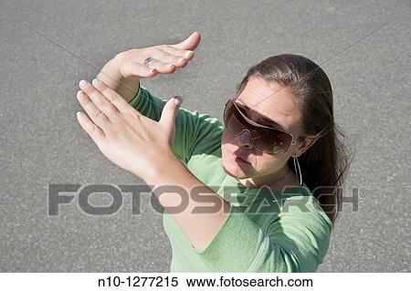 Stock Photography - Young woman, wearing sunglasses, blocking the sun with her hands. Fotosearch
