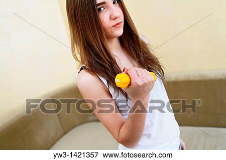 Young woman wearing yellow exercise shirt doing arm curls looking at bicep View Large Photo Image Stock Photo - Young woman wearing yellow exercise shirt doing arm curls looking at bicep. Fotosearch