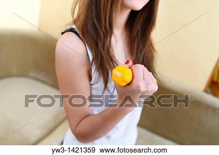 Stock Photo - Young woman wearing yellow exercise shirt doing arm curls looking at bicep. Fotosearch