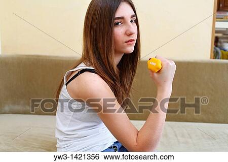 Young woman wearing yellow exercise shirt doing arm curls looking at bicep View Large Photo Image Stock Photograph - Young woman wearing yellow exercise shirt doing arm curls looking at bicep. Fotosearch