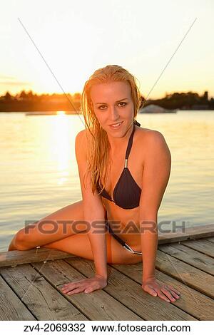 Young woman with a bikini sitting on a jetty at a lake in Austria by sunset View Large Photo Image Stock Image - Young woman with a bikini sitting on a jetty at a lake in Austria by sunset. Fotosearch