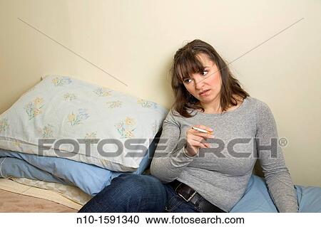 Stock Image - Young woman, with a cigarette, sitting on her bed. Fotosearch