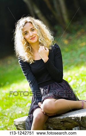 Young woman with a curly hair is sitting in the park View Large Photo Image Stock Image - Young woman with a curly hair is sitting in the park. Fotosearch