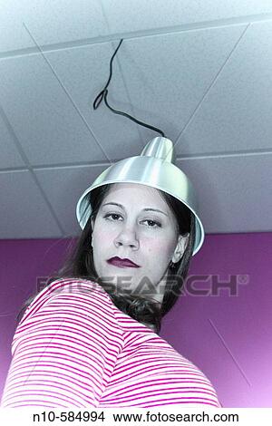 Young woman with a metal hood, which is attached to a wire dropping down from the ceiling, setting on her head. View Large Photo Image Picture - Young woman with a metal hood, which is attached to a wire dropping down from the ceiling, setting on her head.. Fotosearch