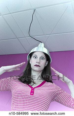 Stock Photography - Young woman with a metal hood, which is attached to a wire dropping down from the ceiling, setting on her head.. Fotosearch