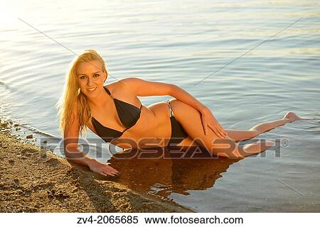 Stock Photography - Young woman with bikini lying at the shore of a lake in Austria.. Fotosearch