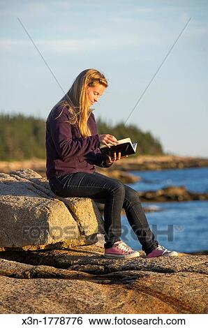 Stock Photograph - Young woman with journal at sunset, Schoodic Peninsula, Maine, USA. Fotosearch
