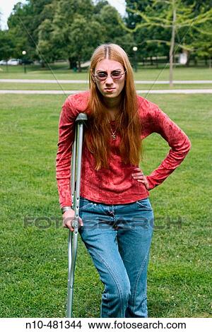 Young woman, with long hair and wearing glasses, standing with a crutch at a park View Large Photo Image Picture - Young woman, with long hair and wearing glasses, standing with a crutch at a park. Fotosearch