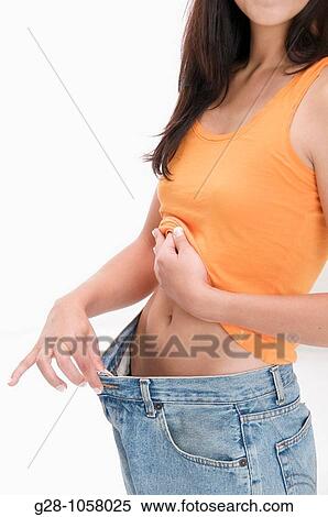 Stock Photography - young woman with long hair trying on too big jeans, she has slimmed after a diet. Fotosearch