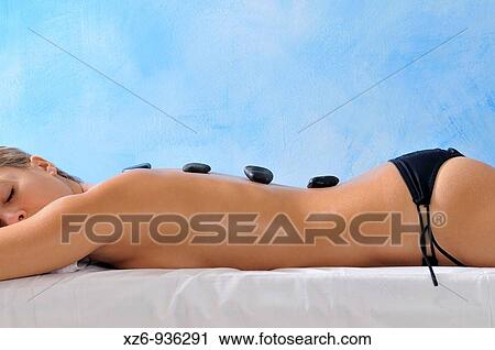 Stock Image - Young woman with therapeutic hot stones on her back. Fotosearch