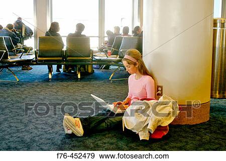 Stock Photo - Young woman working on laptop in airport. Fotosearch
