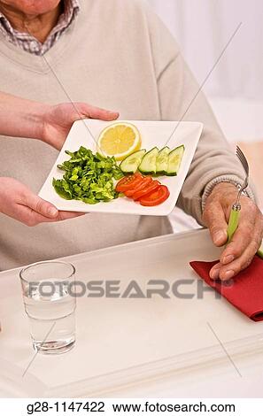 Stock Image - young woman's hands serving a meal to a senior person. Fotosearch