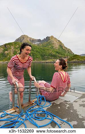 Stock Photo - young women, dressed with an old-fashioned swimming costume, bathing into the icy water of the fjord, Hamn i Senja Hotel, Senja island, County of Troms, Norway, Northern Europe. Fotosearch