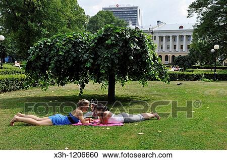Stock Image - young women lying in the grass of a park, Tallinn, estonia, northern europe. Fotosearch