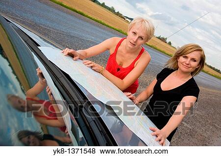 Stock Photo - Young women on road trip and looking road map by car. Fotosearch