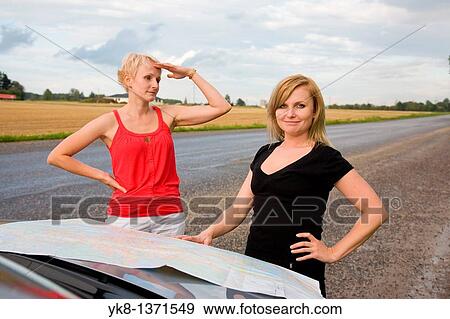 Stock Photo - Young women on road trip and looking road map by car. Fotosearch