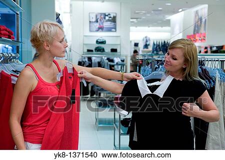 Stock Image - Young women shopping and comparing different clothes in store. Fotosearch